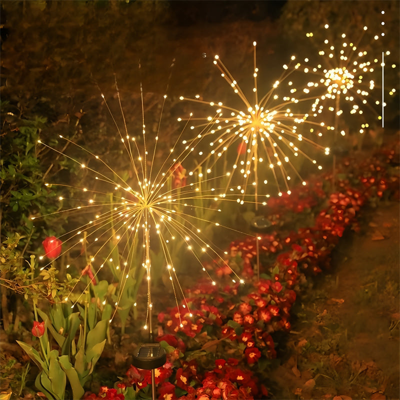 Solar firework lights glowing warm white in a garden flower bed at night